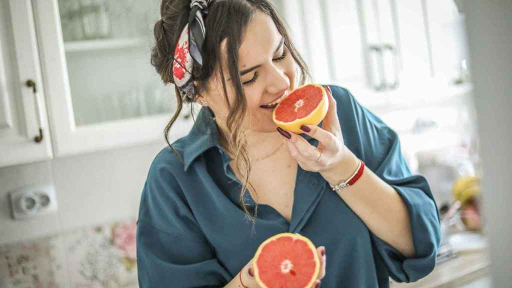 Mujer comiendo la mitad de un pomelo.