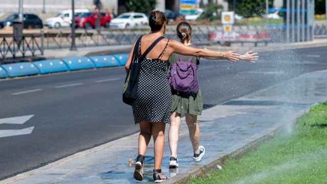 Dos mujeres se mojan con unos chorros de regadío en agosto de 2023, en Madrid (España).
