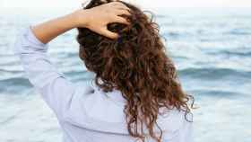 Mujer de espaldas frente al mar tocándose el pelo.