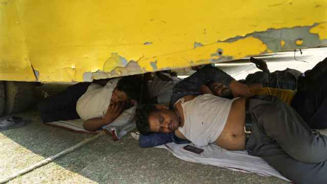 Los trabajadores se resguardan del calor debajo de un autobús en la India.