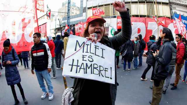 Una manifestante con un cartel que dice Milei es hambre, mientras protesta ante la llegada del presidente argentino.