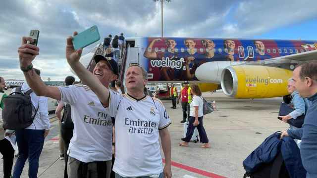 Aficionados del Real Madrid se hacen una foto con el avión del Barça detrás.