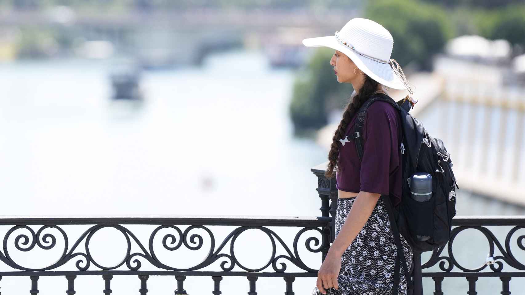 Una joven se protege del sol con un sombrero mientras pasea por el Puente de Triana.