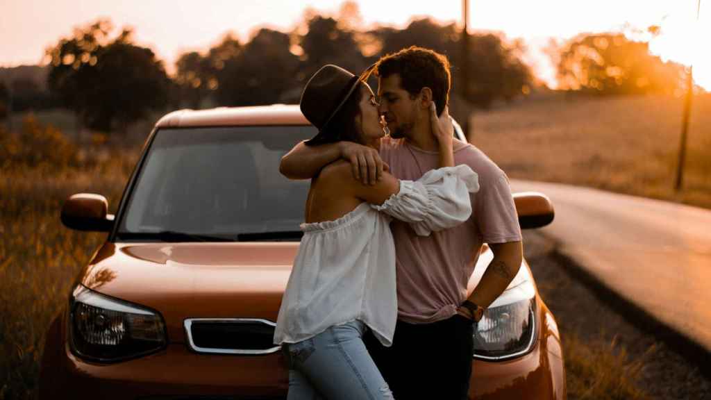 Pareja apoyada en un coche besándose.