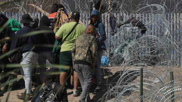 Migrantes esperan entre los alambres de púas cerca del muro que separa la frontera de EEUU en Ciudad Juárez.