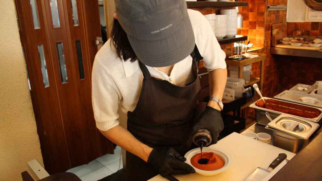 Heba, siempre con su gorra, prepara detrás de la barra muhammara de pimiento rojo.