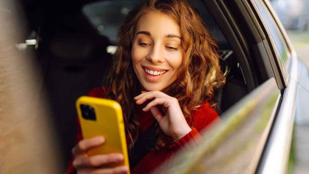 Mujer sonriente con el teléfono móvil mientras viaja en coche.