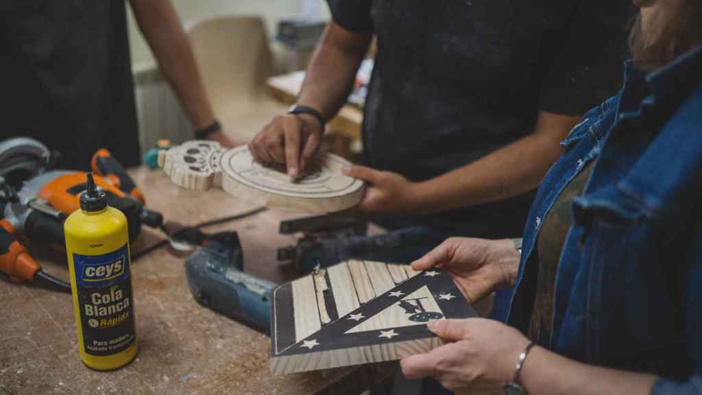 Uno de los menores del taller de carpintería le enseña a Pilar López, gerente de ARRMI, cómo tallan las piezas de madera.