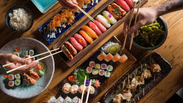 Varias personas comiendo sushi de diferentes tipos.