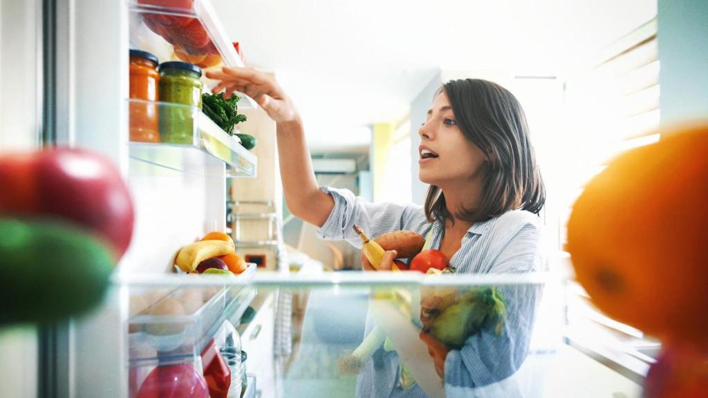 Mujer cogiendo del frigorífico frutas y verduras.