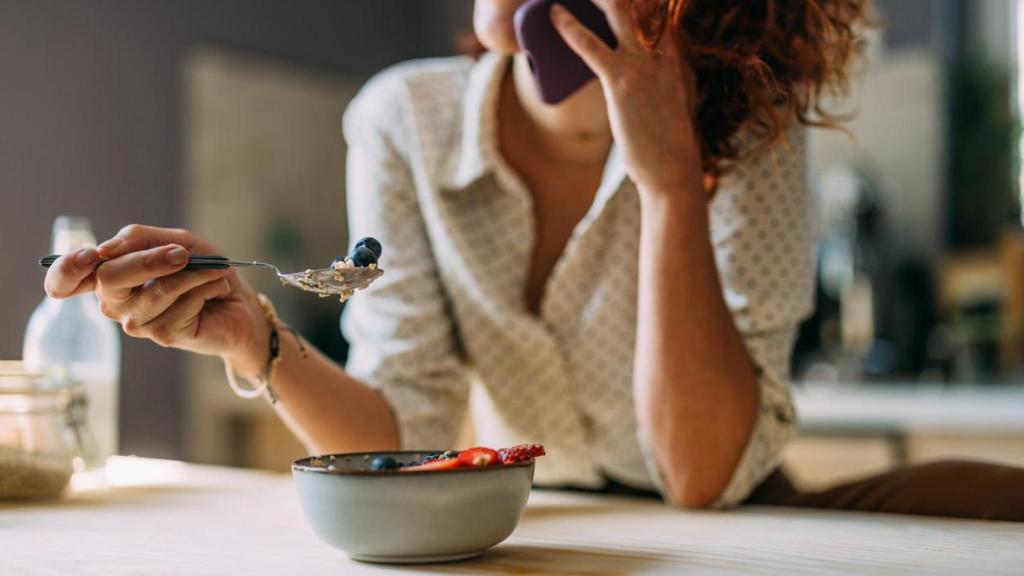 Mujer comiendo yogur con fruta mientras habla por teléfono.