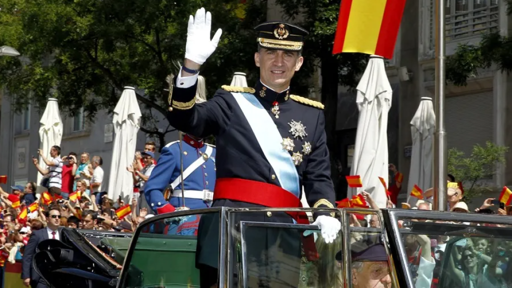 El rey Felipe VI saluda a su paso por la Carrera de San Jerónimo en su trayecto hacia el Palacio Real en un Rolls Royce descapotable.