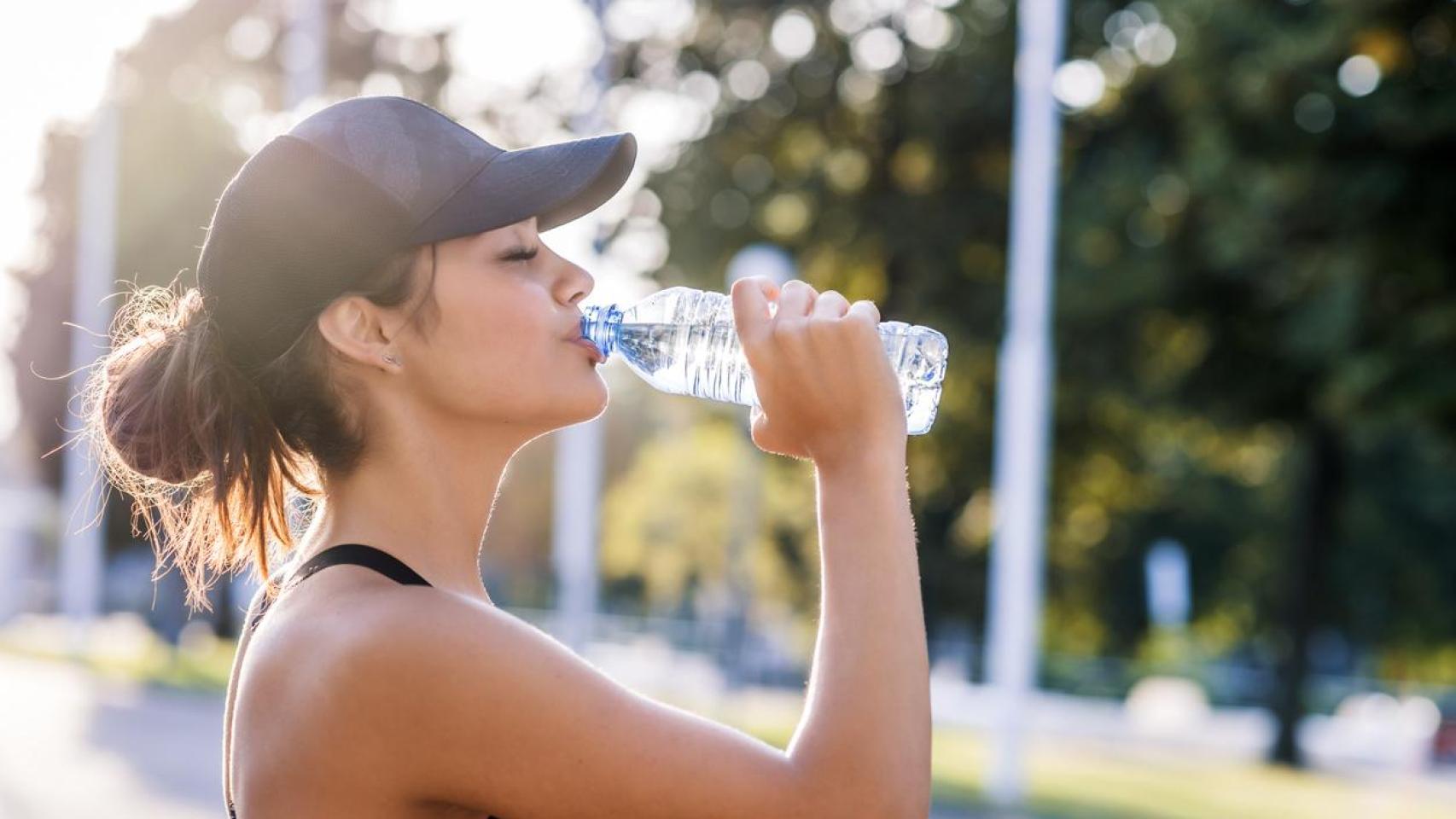 Mujer con gorra bebiendo agua tras hacer deporte.