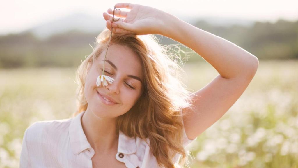 Mujer sonriente, con los ojos cerrados y una margarita en la mano.