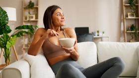 Mujer con ropa de deporte comiendo en el sofá de su casa.