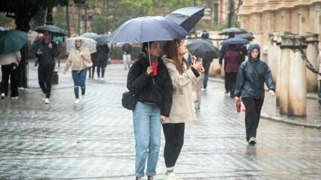 Dos turistas se protegen de la lluvia frente a la Catedral de Sevilla.