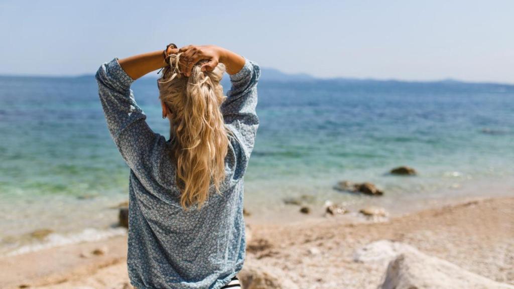 Mujer de espaldas frente al mar tocándose su melena ondulada.