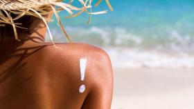 Mujer con sombrero frente al mar y un signo de exclamación pintado con crema en el hombro.