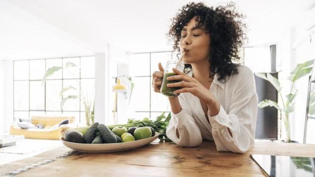 Mujer en la cocina tomando un smoothie vegetal.