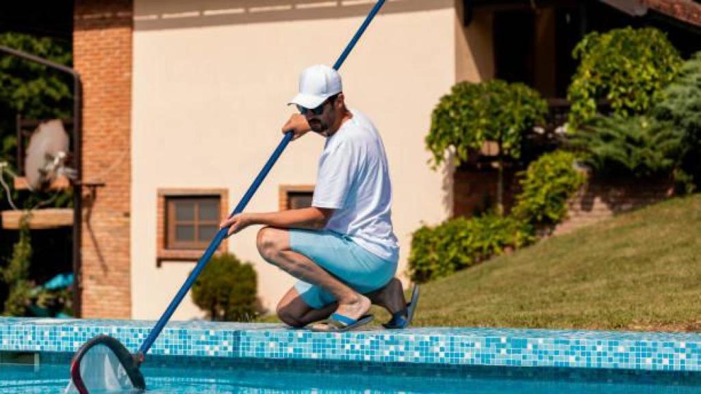 Un hombre limpiando su piscina.