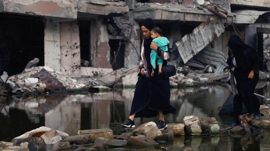 Una mujer sostiene a un niño mientras camina junto a edificios destruidos en un ataque israelí en Jan Yunís.