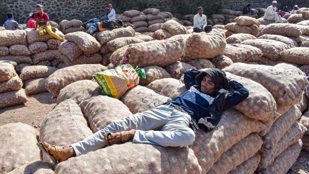 Agricultores descansan sobre sacos de cebollas en un mercado de la India.