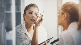 Mujer maquillándose los ojos frente al espejo.