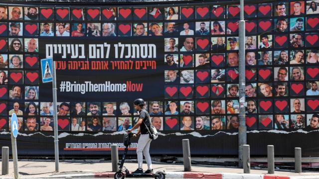 Una persona en patinete junto a carteles con fotografías de rehenes secuestrados durante el mortal ataque del 7 de octubre por parte de Hamas, en Jerusalén.