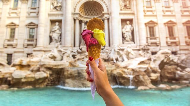 Una mano sostiene un helado frente a la Fontana di Trevi de Roma.