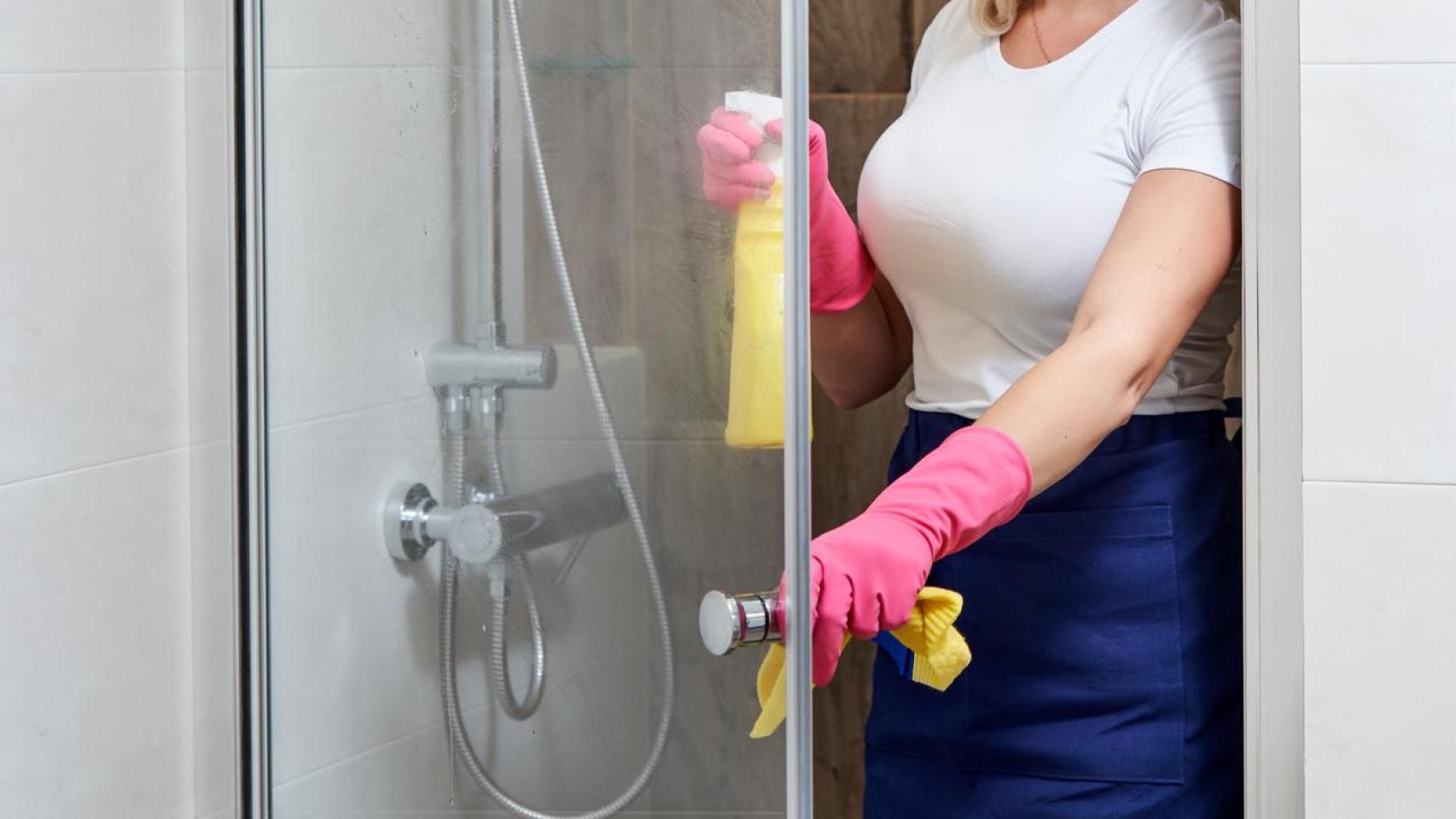 Una mujer limpiando la mampara de la ducha.