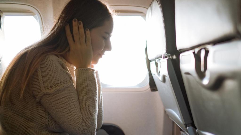 Una persona sufriendo dolor de oídos en el interior de un avión.