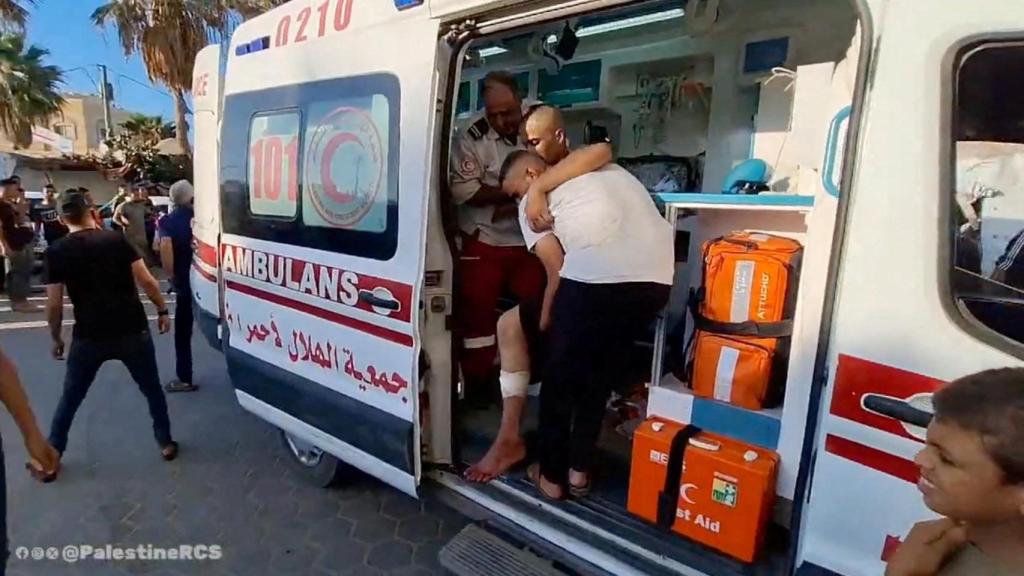 La gente ayuda a un hombre mientras miembros de la Media Luna Roja Palestina transportan a los heridos al hospital de los Mártires de Al-Aqsa.