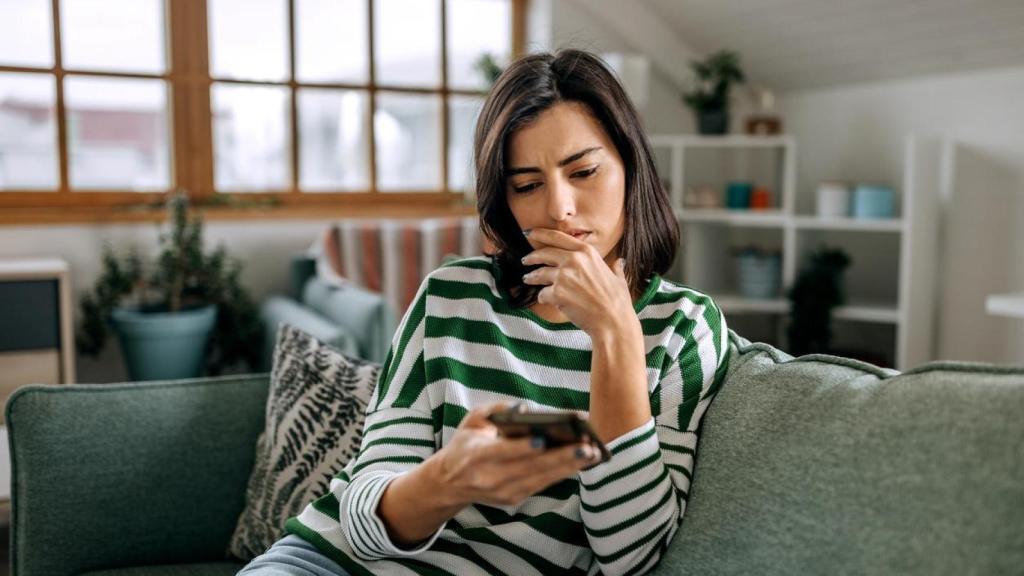 Mujer mirando el teléfono con gesto contrariado.