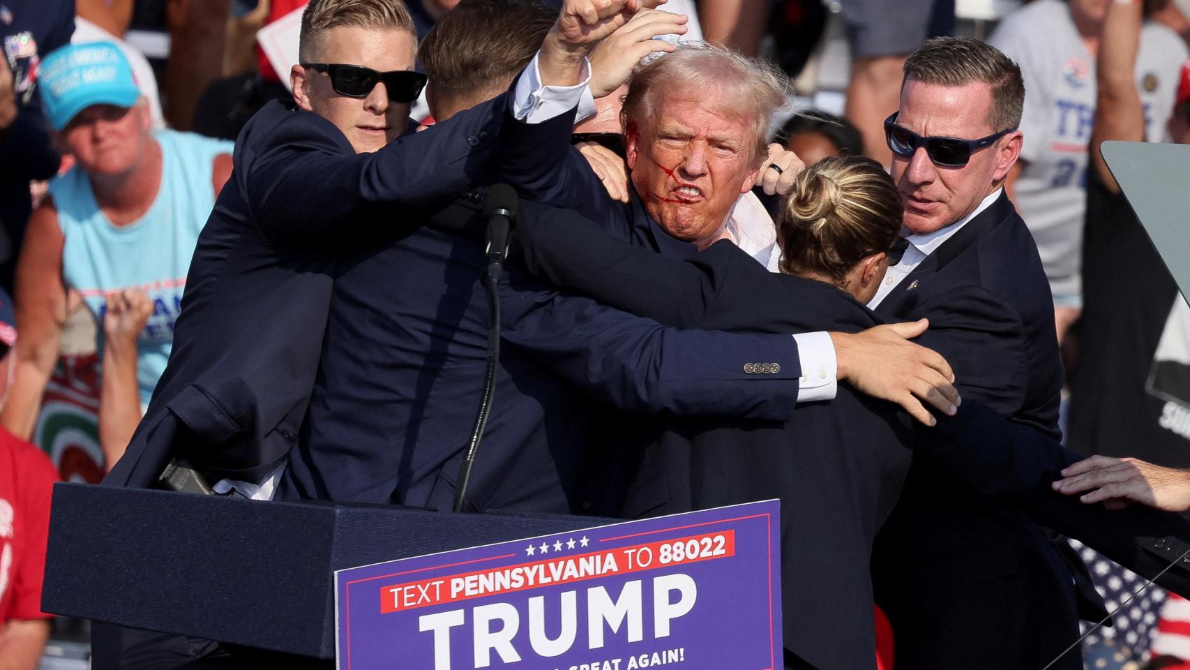 El candidato presidencial republicano y expresidente estadounidense, Donald Trump, hace un gesto con el rostro ensangrentado mientras es asistido por personal del Servicio Secreto de Estados Unidos, después de que le dispararan en la oreja derecha durante un mitin de campaña en el Butler Farm Show en Butler, Pensilvania.