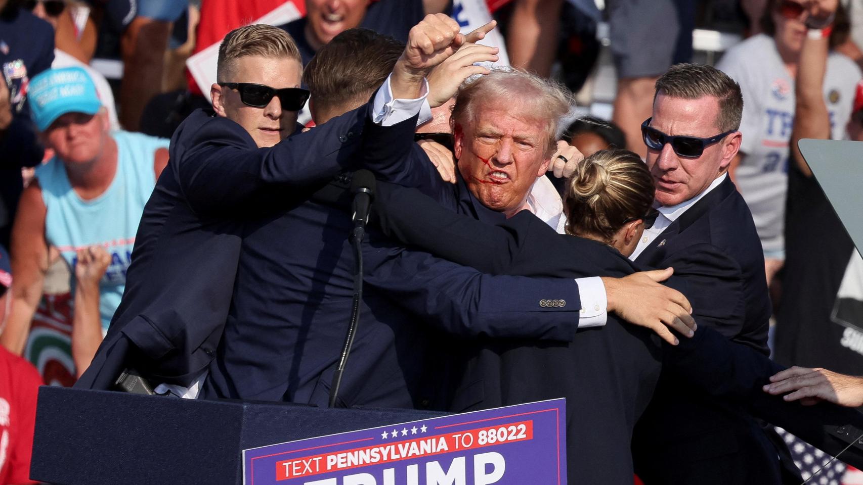 El candidato presidencial republicano y expresidente estadounidense, Donald Trump, hace un gesto con el rostro ensangrentado mientras es asistido por personal del Servicio Secreto de Estados Unidos, después de que le dispararan en la oreja derecha durante un mitin de campaña en el Butler Farm Show en Butler, Pensilvania.