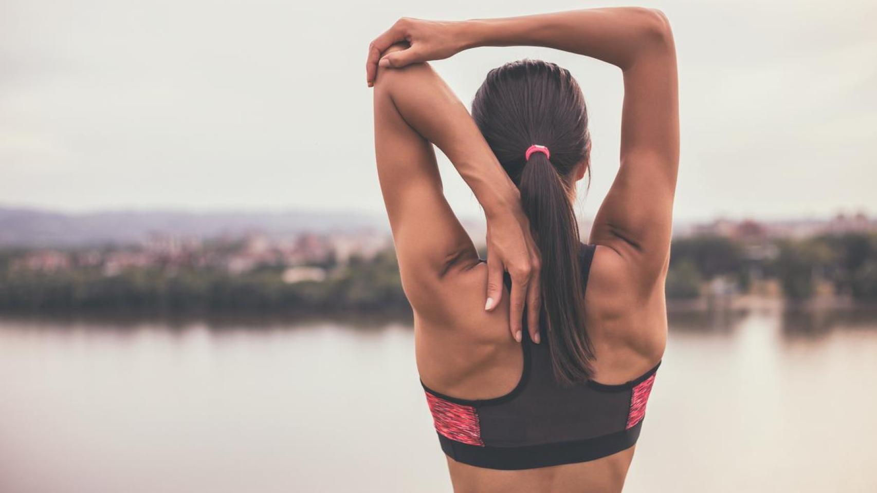 Mujer de espaldas con ropa de deporte estirándose.