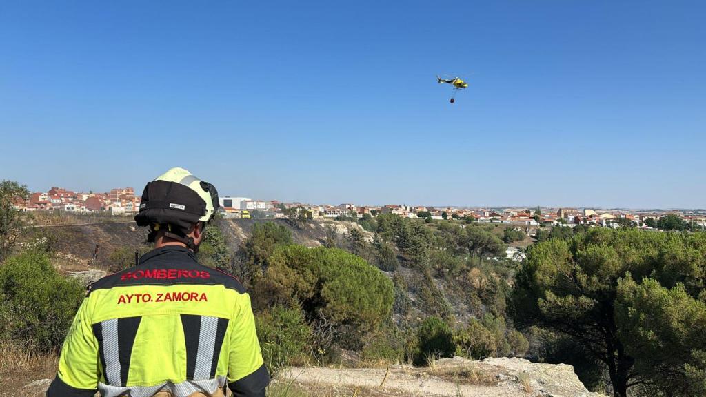Un efectivo de los Bomberos de Zamora desplegado en la zona del incendio, y en el cielo, el helicóptero de la Junta