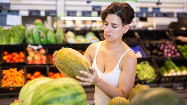 Una compradora sosteniendo un melón en el supermercado.