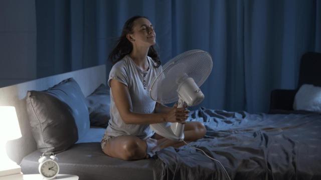 Mujer con un ventilador en la cama.