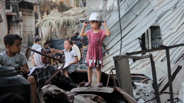 Una niña palestina con una olla en la cabeza recibe comida durante conflicto en Gaza, julio de 2024.