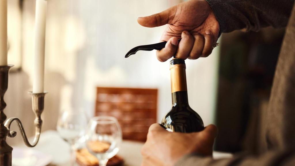 Una persona abre una botella de vino con un sacacorchos