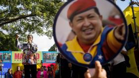 El presidente de Venezuela, Nicolás Maduro, habla ante sus seguidores y uno de ellos sube una pancarta de Chávez.