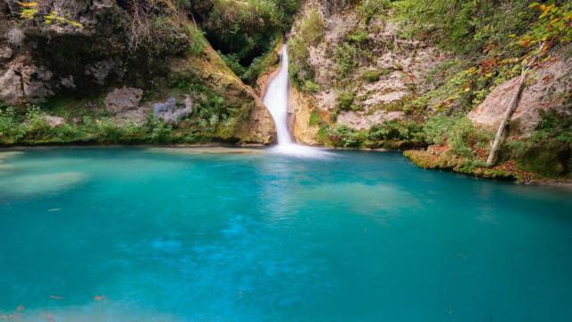 Una poza de aguas cristalinas con cascada y rodeada de vegetación.