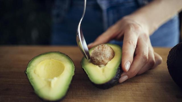 Mujer quitando la semilla del aguacate con una cuchara.