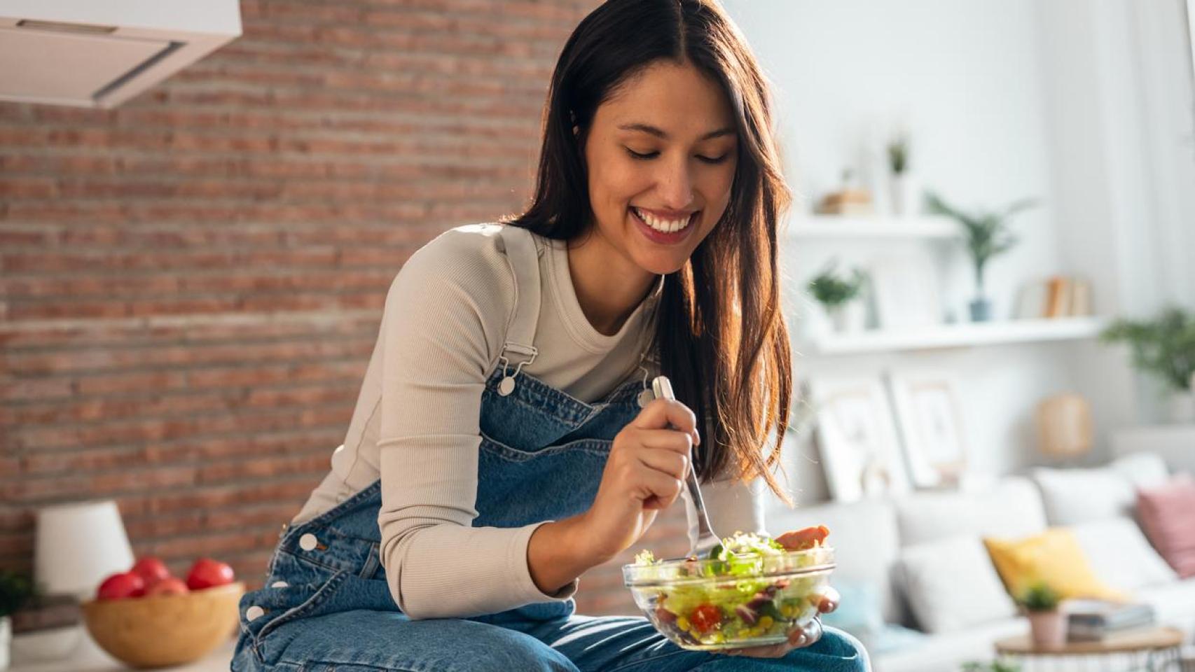 Mujer sentada en la encima de la cocina comiendo una ensalada.