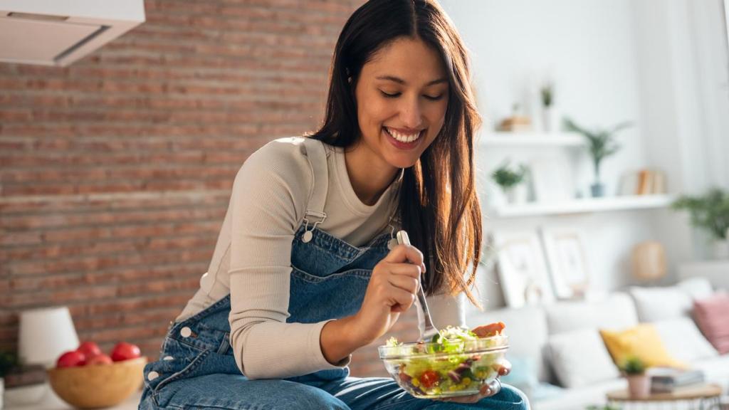 Mujer sentada en la encima de la cocina comiendo una ensalada.