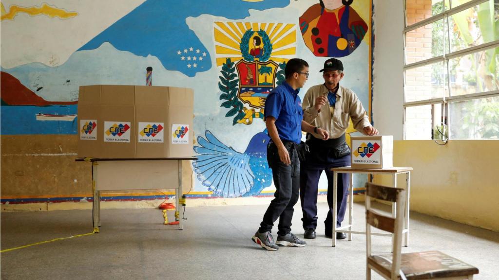 Dos voluntarios preparan una mesa electoral en un colegio de Caracas, antes de las elecciones.