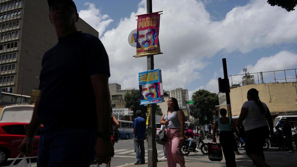 Residentes venezolanos pasean junto a carteles con la imagen Nicolás Maduro, en las calles de Caracas.