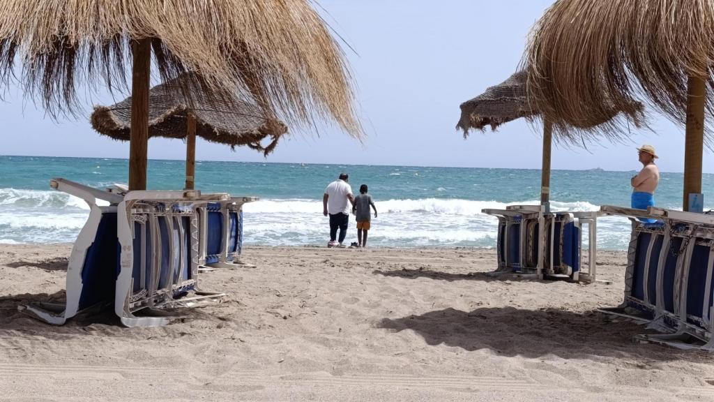 El hermano pequeño de Emmanuel mete los pies en la playa durante el operativo de búsqueda, acompañado por el intérprete de Servicios Sociales de Cartagena.