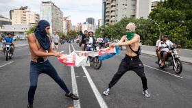 Dos manifestantes en Venezuela intentar romper un cartel electoral de Nicolás Maduro.